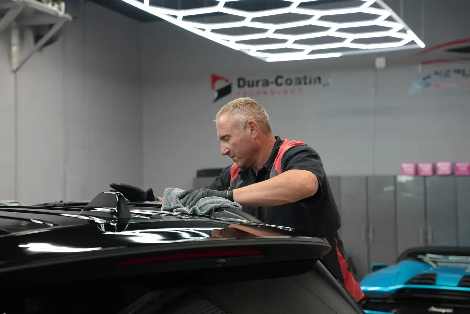 A Naples Ceramic Coatings technician finishing a coated car in front of the Dura-Coating Technology sign